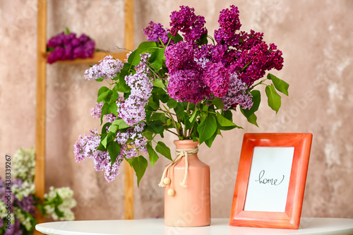 Vase with lilac flowers and frame on table near color wall