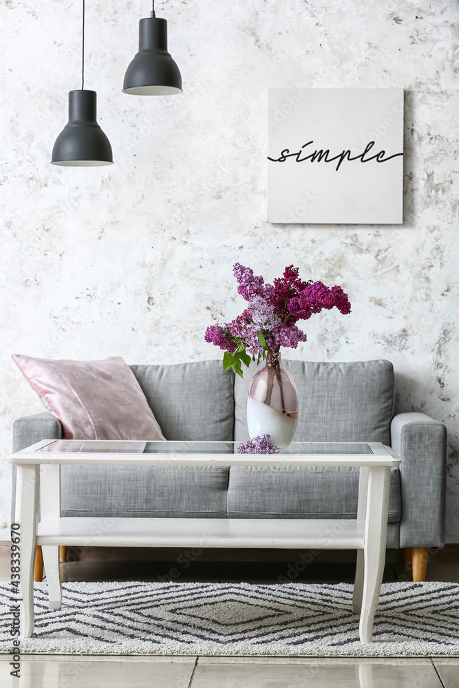 Cozy sofa and vase with lilac flowers near light wall