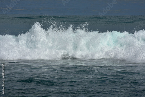 An ocean shorebreak in front view. Big beautiful green blue wave splashing with backwave and ready to break out. White foam sliding over sand. Bright sun shining on blue sky.