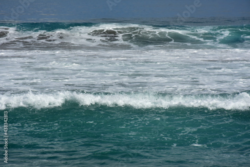 An ocean shorebreak in front view. Big beautiful green blue wave splashing with backwave and ready to break out. White foam sliding over sand. Bright sun shining on blue sky.