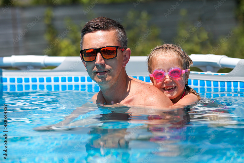 Father in sunglasses swims in the pool with his daughter. Dad and little girl in swimming goggles swim in the pool. A happy man and a child in the water.