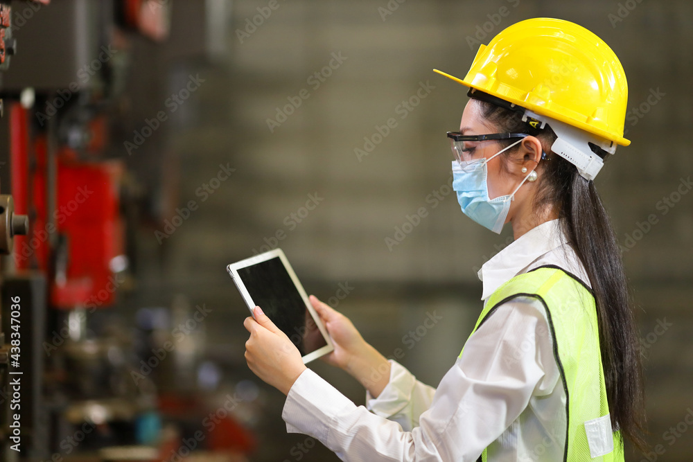 Asian woman engineering manager with facial mask in safety hard hat and reflective cloth is inspecting inside the factory using digital tablet for new normal and covid-19 pandemic Asian woman engineering manager with facial mask in safety hard hat and reflective cloth is inspecting inside the factory using digital tablet for new normal and covid-19 pandemic