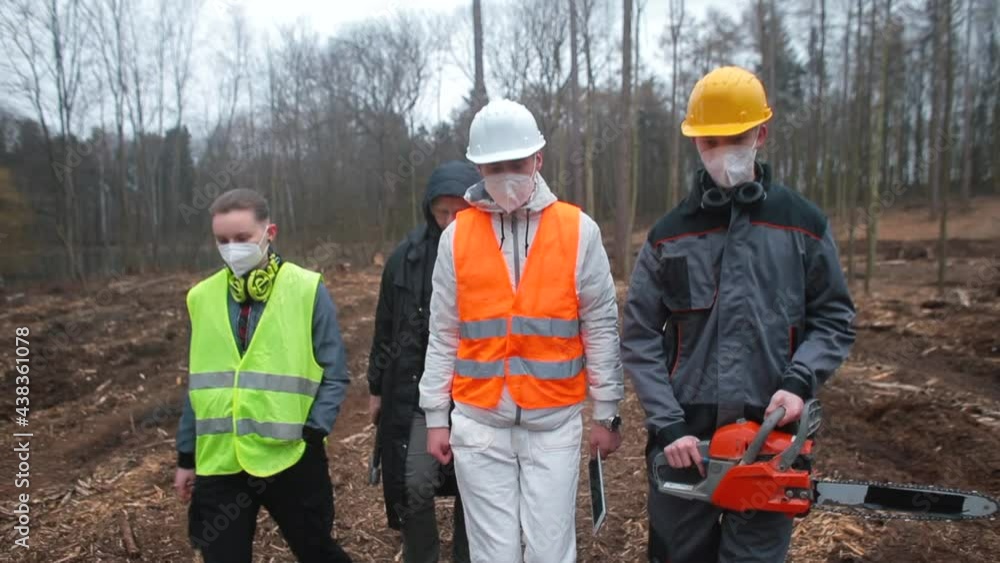 A group of logging workers are moving through the forest. They hold tools, an ax, a saw, a tablet in their hands. Discussion of work issues in a team of workers. Communication. A group of logging workers are moving through the forest. They hold tools, an ax, a saw, a tablet in their hands. Discussion of work issues in a team of workers. Communication.