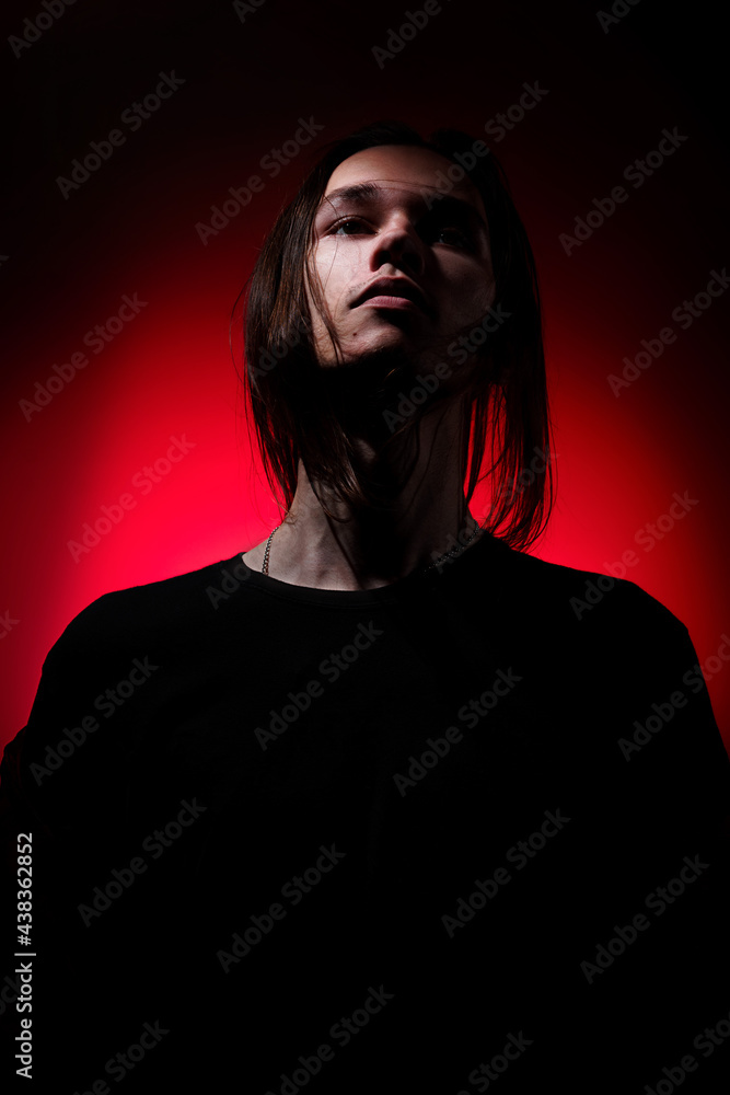 Fototapeta premium Portrait of a young man with long hair on a red and black background