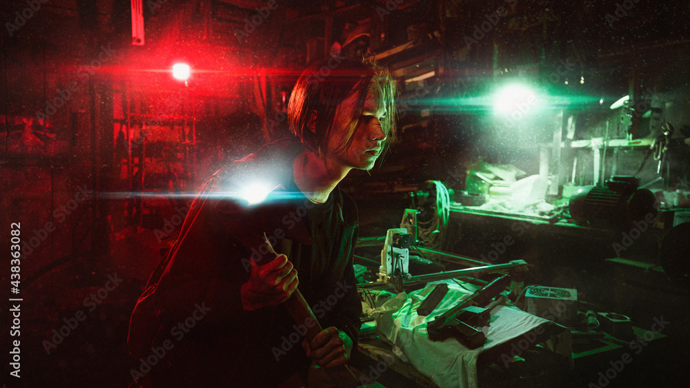 A survivor of the post-apocalypse man with an axe and flashlights hides in an abandoned dusty basement, illuminated by red and green light