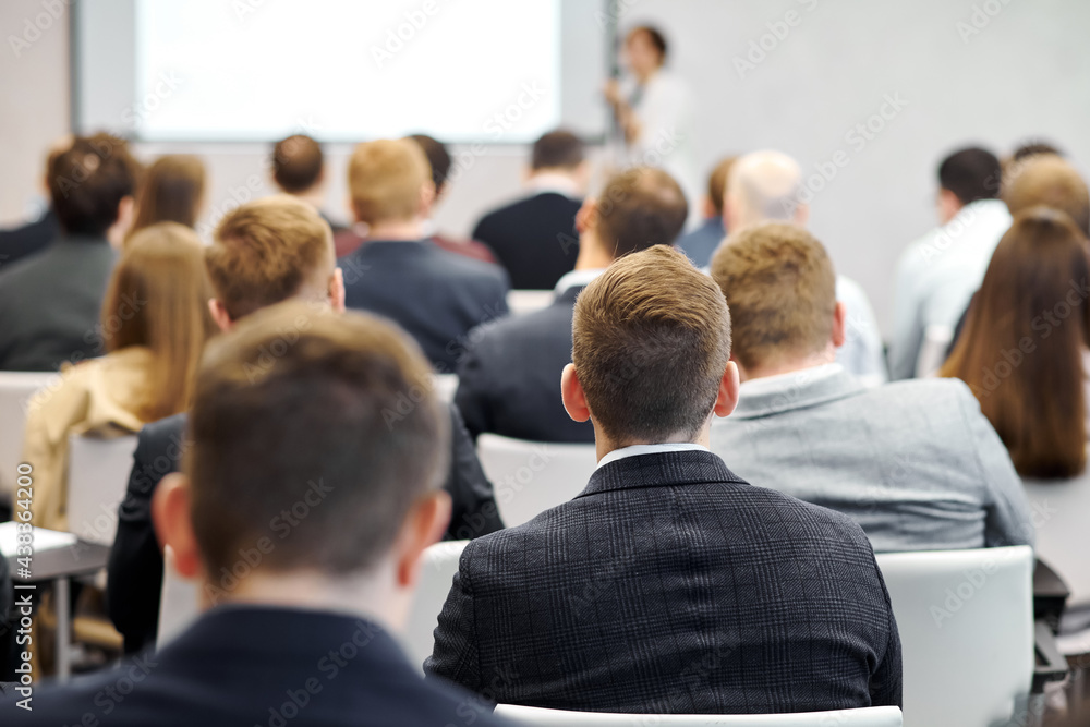 Group of people at the business conference, back view. Row of business people listen to the speaker on the forum or at seminar in modern conference room.