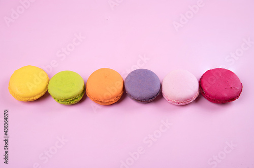 Lined up in a row of pastel-colored macaroons cookies on a pink paper background. Copy space