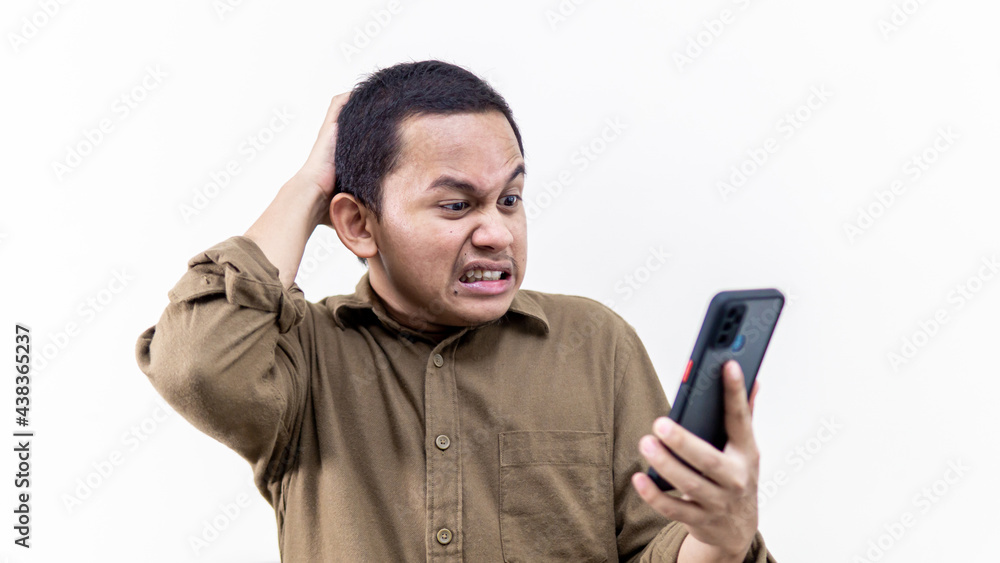 A portrait of an Asian Malay man getting mad and annoying while holding a smartphone on isolated white background. Received bad, failed, unlucky and problem news. Man stressed out over the phone. A portrait of an Asian Malay man getting mad and annoying while holding a smartphone on isolated white background. Received bad, failed, unlucky and problem news. Man stressed out over the phone.