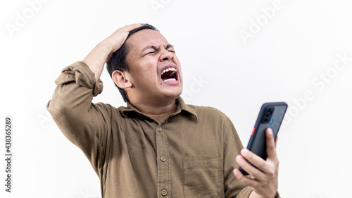 Fotografie A portrait of an Asian Malay man screaming out while holding a smartphone on isolated white background