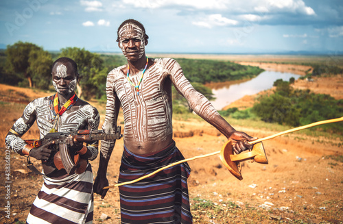 Two men with a machine gun standing near Omo river on Karo tribe village. Omo Valley, Ethiopia photo