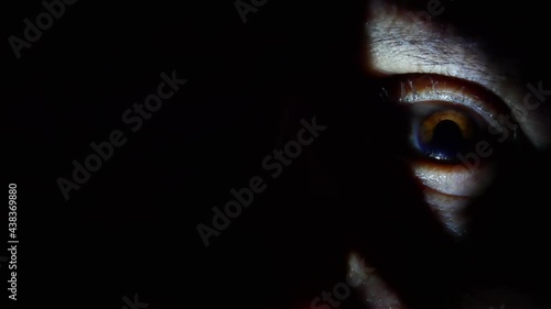 Close up mysterious eye in the night with chiaroscuro, freezing and frightening atmosphere, creepy man's face hidden in the dark, spy eye 
