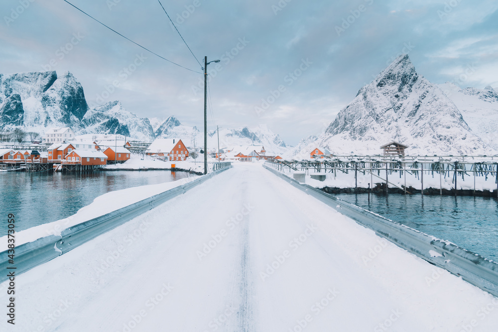 Road running to buildings in village on shore and hills in snow Road running to buildings in village on shore and hills in snow
