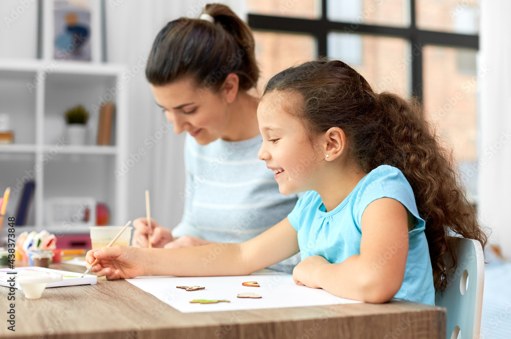 family, hobby and leisure concept - happy smiling mother spending time with her little daughter drawing or painting wooden chipboard cutouts with colors at home family, hobby and leisure concept - happy smiling mother spending time with her little daughter drawing or painting wooden chipboard cutouts with colors at home
