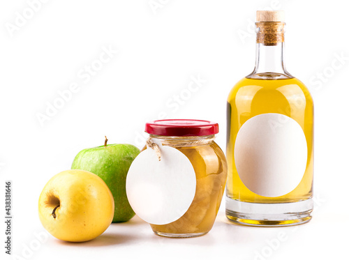 Fresh apples, bottle with fruit brandy and jam. Glass bottle and jar with oval labels, green and yellow color apples isolated on white background. Homemade fruit alcohol and jam concept.