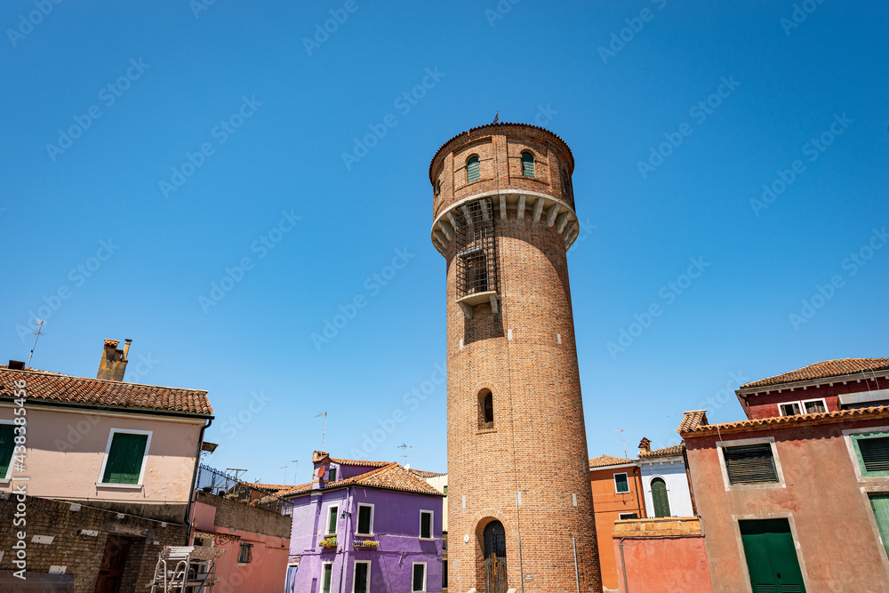 Old water tower of the aqueduct in Burano island and small multi colored houses (bright colors) in a sunny spring day. Venice lagoon, UNESCO world heritage site, Veneto, Italy, southern Europe.