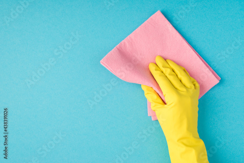 Top view photo of hand in yellow rubber glove holding pink viscose rag on isolated pastel blue background with copyspace