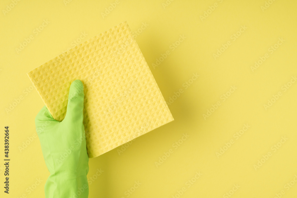 Above pov photo of reusable cleaning cellulose sponge and green gloves isolated on the yellow background Above pov photo of reusable cleaning cellulose sponge and green gloves isolated on the yellow background