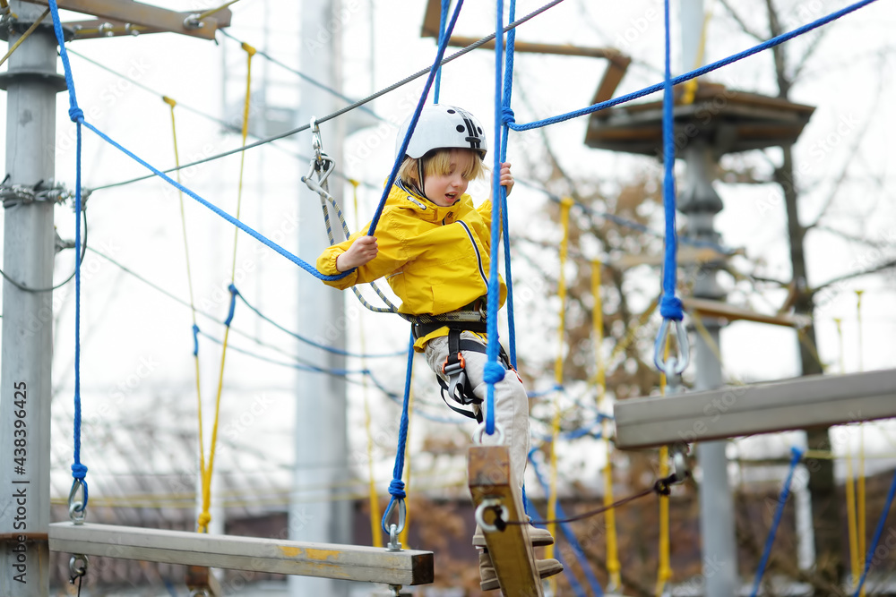 Fototapeta premium Cute boy having fun in Adventure Park for children amoung ropes, stairs, bridges. Frightened child overcomes his fear. Outdoor climbing playground in public park. Activity entertainment for kids