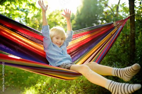 Cute little blond caucasian boy having fun with multicolored hammock in backyard or outdoor playground. Summer active leisure for kids. Child on hammock. Activities for children outdoors