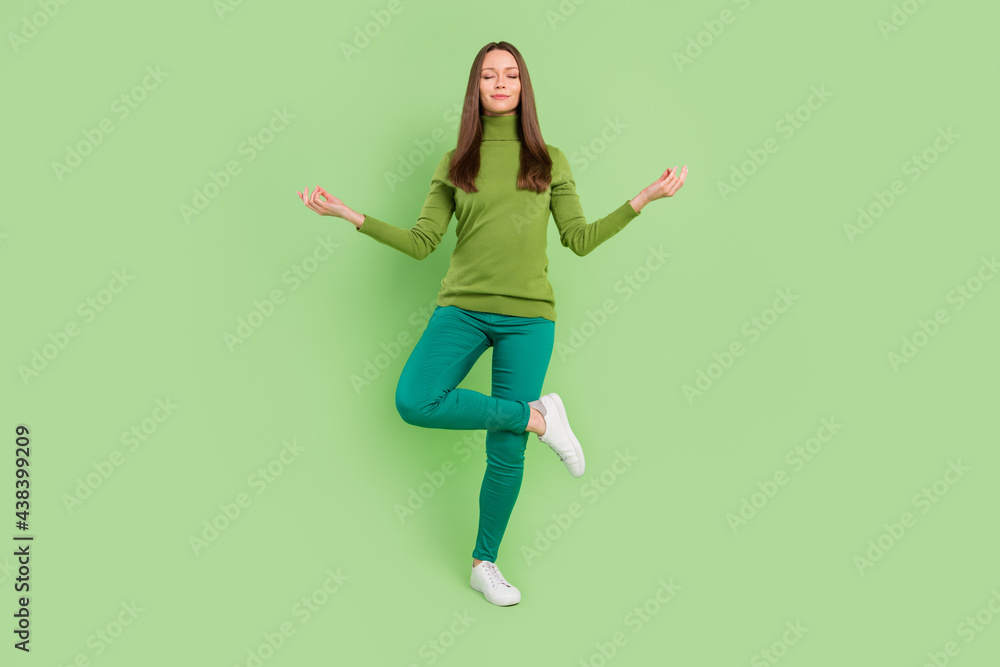 Full length photo of charming calm young woman asana meditation yoga smile isolated on green color background Full length photo of charming calm young woman asana meditation yoga smile isolated on green color background