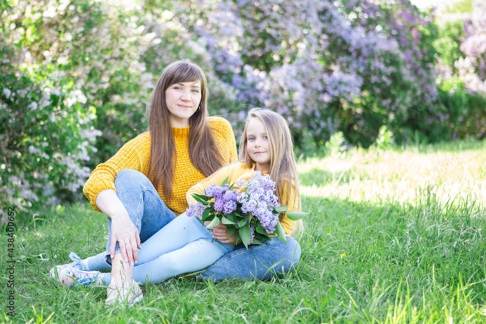 Mom and daughter laughing and hugging sitting on a blanket in the park in a clearing. The concept of a happy family, friendship, and love. Outdoor activities Mom and daughter laughing and hugging sitting on a blanket in the park in a clearing. The concept of a happy family, friendship, and love. Outdoor activities