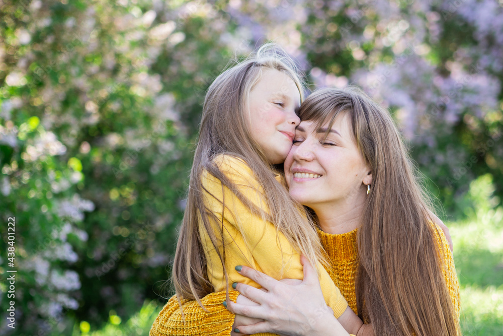 Fototapeta premium Mom and daughter laughing and hugging sitting on a blanket in the park in a clearing. The concept of a happy family, friendship, and love. Outdoor activities