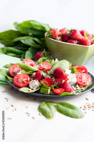 Salad with strawberries, cherry tomatoes, sunflower seeds, spinach and feta cheese on gray background