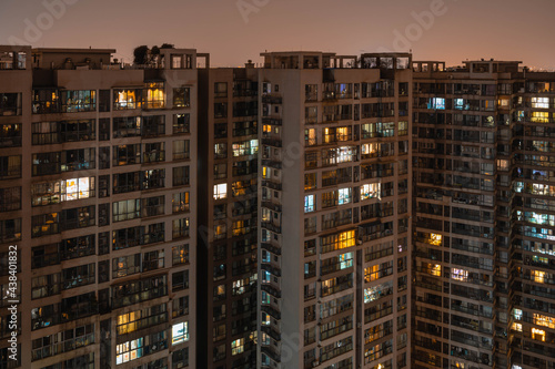 Long exposure night aerial view on residential buildings complex compound. Tall skyscrapers thousands of apartments light illuminates from windows. Small square park inside community. City development