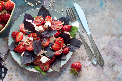 Salad with strawberries, cherry tomatoes, sunflower seeds, basil and feta cheese on gray background. Top view