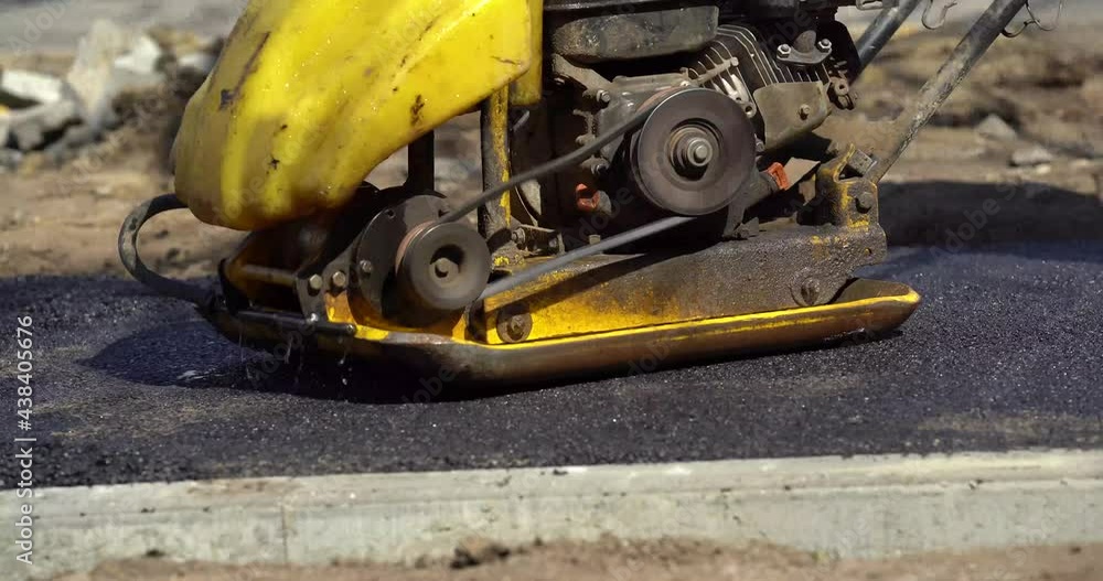 Compactor is driving over freshly poured asphalt and compresses it on
