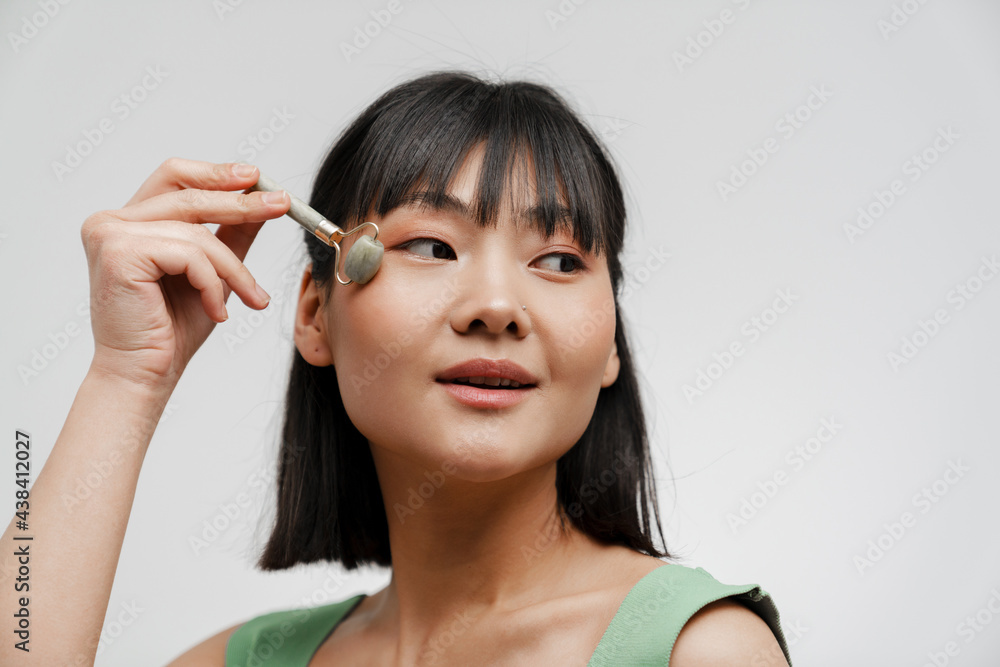 Young asian woman with piercing massaging face with jade roller Young asian woman with piercing massaging face with jade roller