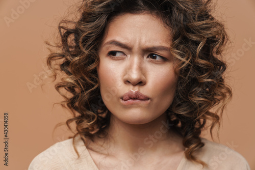 Young curly hispanic woman frowning and looking aside