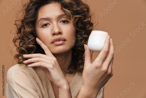 Young curly hispanic woman posing with facial cream