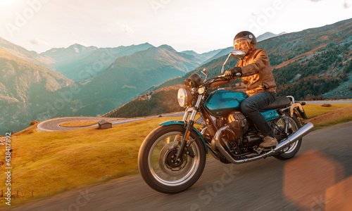 Motorcycle driver riding in Alpine landscape. Lifestyle photo with motion blur effect and copyspace.