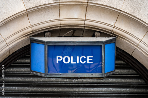 Traditional old fashioned retro blue police sign above arched stone town station door. British police iconic blue coloured lamp with white text attached to wall. photo