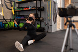 Athletic fitness instructor with a protective mask, gym dumbbell, and balance gym workout exercises live on camera for sportive followers on social media. Home fitness workout class live streaming. 