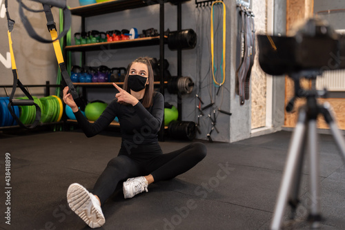 Athletic fitness instructor with a protective mask, gym dumbbell, and balance gym workout exercises live on camera for sportive followers on social media. Home fitness workout class live streaming. 