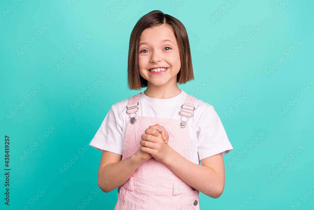 Photo of cheerful happy nice small girl good mood hold hands dream wish isolated on teal color background Photo of cheerful happy nice small girl good mood hold hands dream wish isolated on teal color background