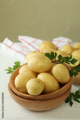 Wooden bowl with young potato on white wooden table