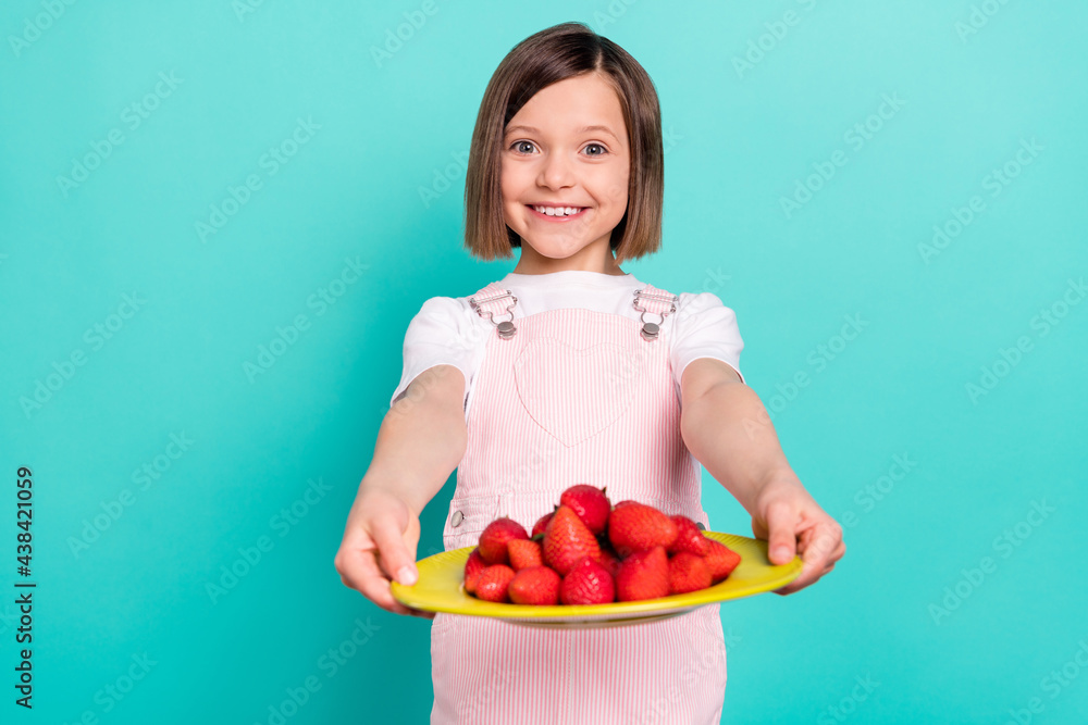 Photo of pretty charming schoolgirl dressed pink overall propose you big plate berries smiling isolated turquoise color background Photo of pretty charming schoolgirl dressed pink overall propose you big plate berries smiling isolated turquoise color background