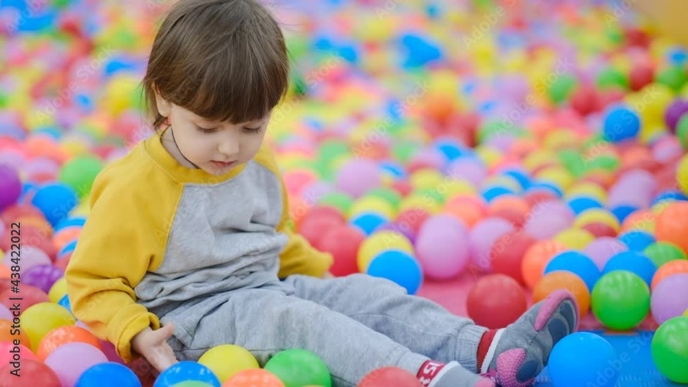 Early childhood development. Toddler Development Center. A cheerful little boy sits in multi-colored plastic balls. Early childhood development. Toddler Development Center. A cheerful little boy sits in multi-colored plastic balls.
