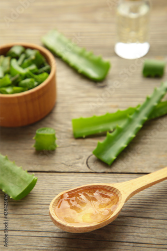 Aloe vera gel on wooden spoon with aloe vera and oil bottle on grey background. Vertical photo