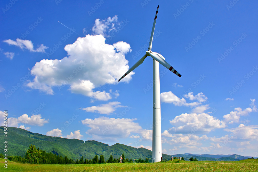 A single windmill in the  foreground against a blue
  sky with white clouds and green mountains in the background, Rytro, Poland