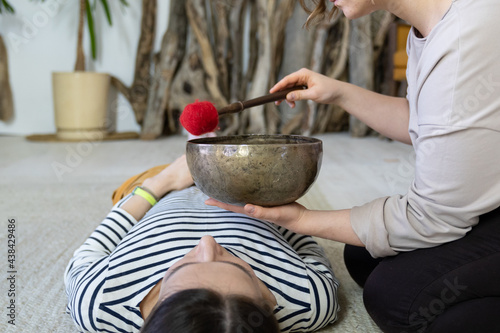 Caucasian masseuse perform tibet sound therapy at relaxed female. Young woman get singing bowls massage. Alternative treatment for mental health, energy recovery, harmony and reducing stress concept