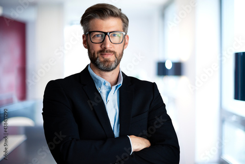 Handsome businessman portrait while standing with arms crossed at the office