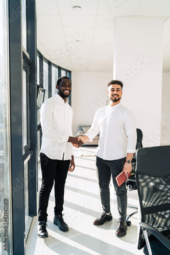 Two multiracial businessmen shake hands in office © Andrii 