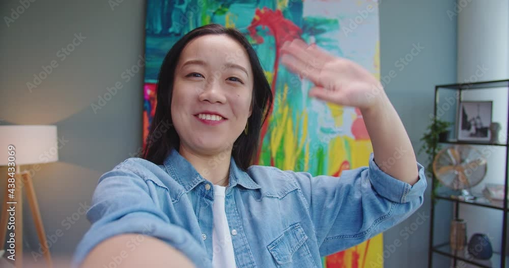POV of joyful happy young pretty Asian female waving hand and smiling speaking on video call on internet at home. Cheerful woman videochatting online on web cam on device. Close up concept POV of joyful happy young pretty Asian female waving hand and smiling speaking on video call on internet at home. Cheerful woman videochatting online on web cam on device. Close up concept