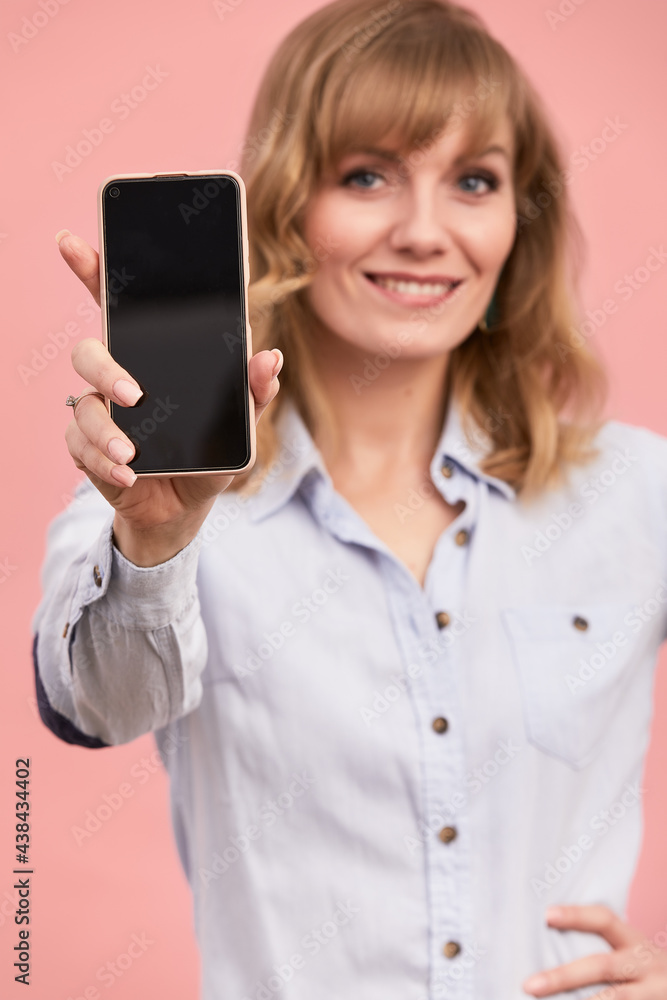 A middle-aged girl with shows on the phone screen, the blonde holds the phone with a screen on a pink background. A middle-aged girl with shows on the phone screen, the blonde holds the phone with a screen on a pink background.