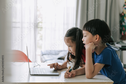 Asian twins boy and girl helping each other to study on line at home during pandemic.