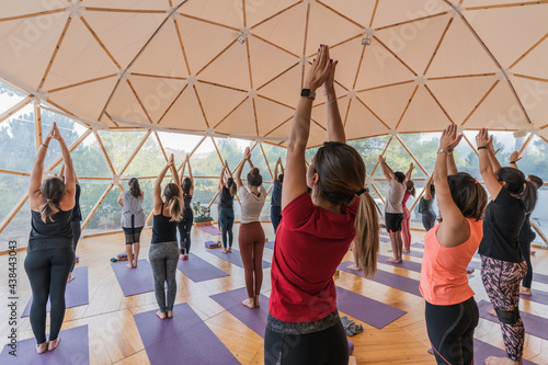 People stretching up with raised hands on yoga mats in domed hal photo
